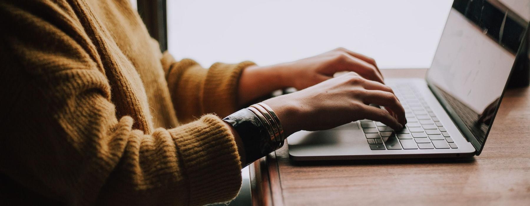 woman types on her laptop near large window